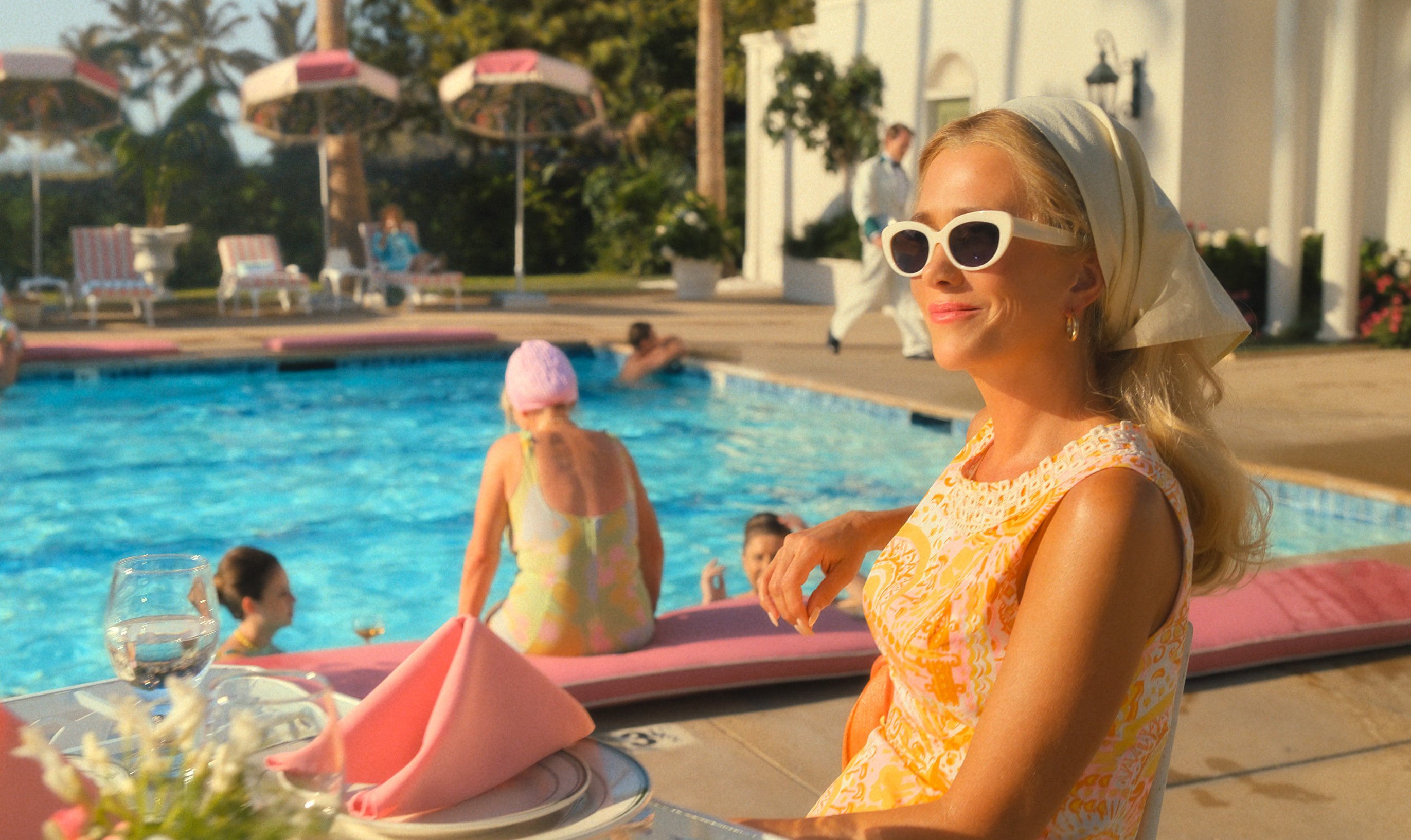 a woman wearing sunglasses sits at a table by a pool