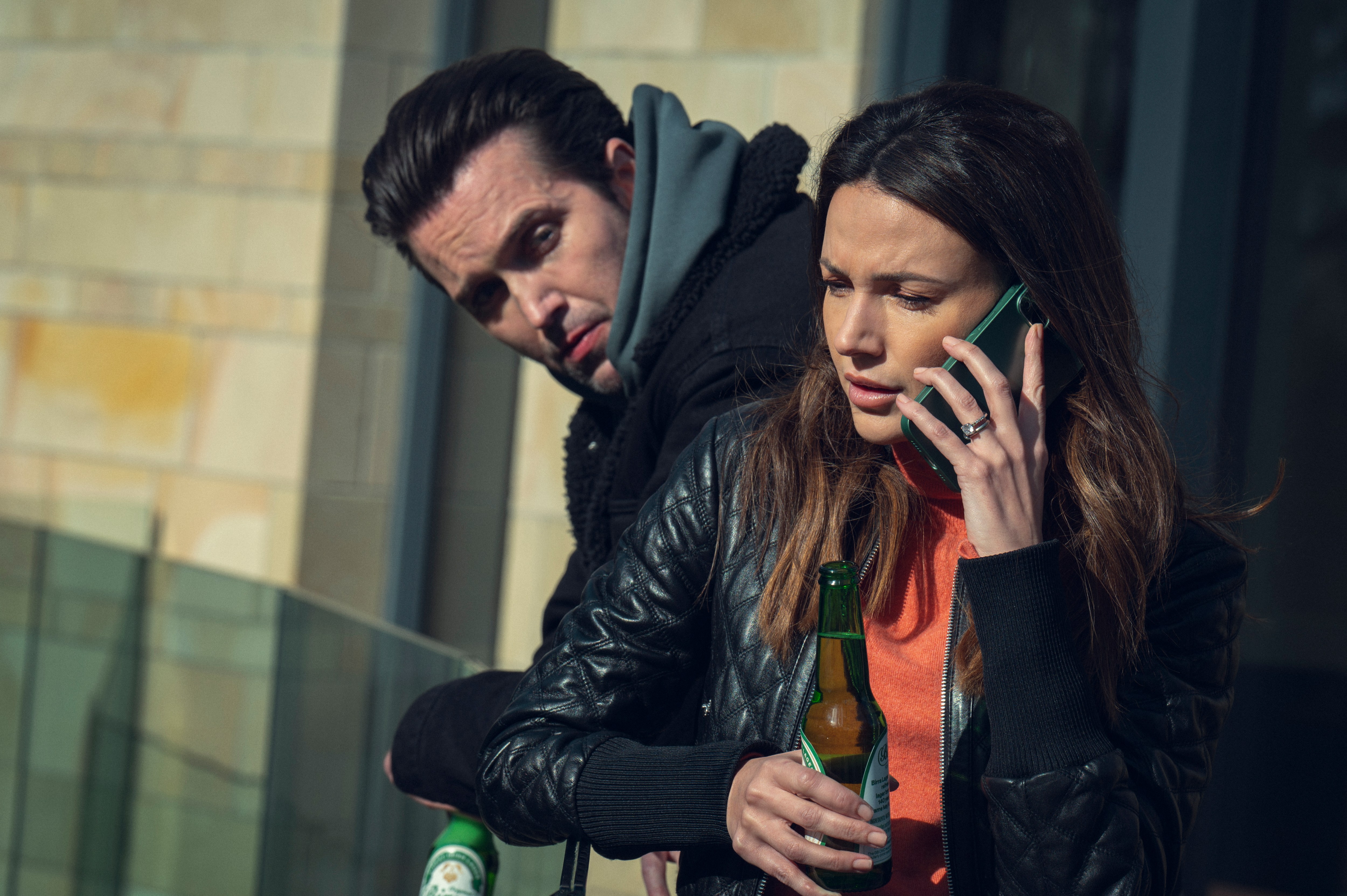 a woman talking on a cell phone while holding a bottle of heineken beer