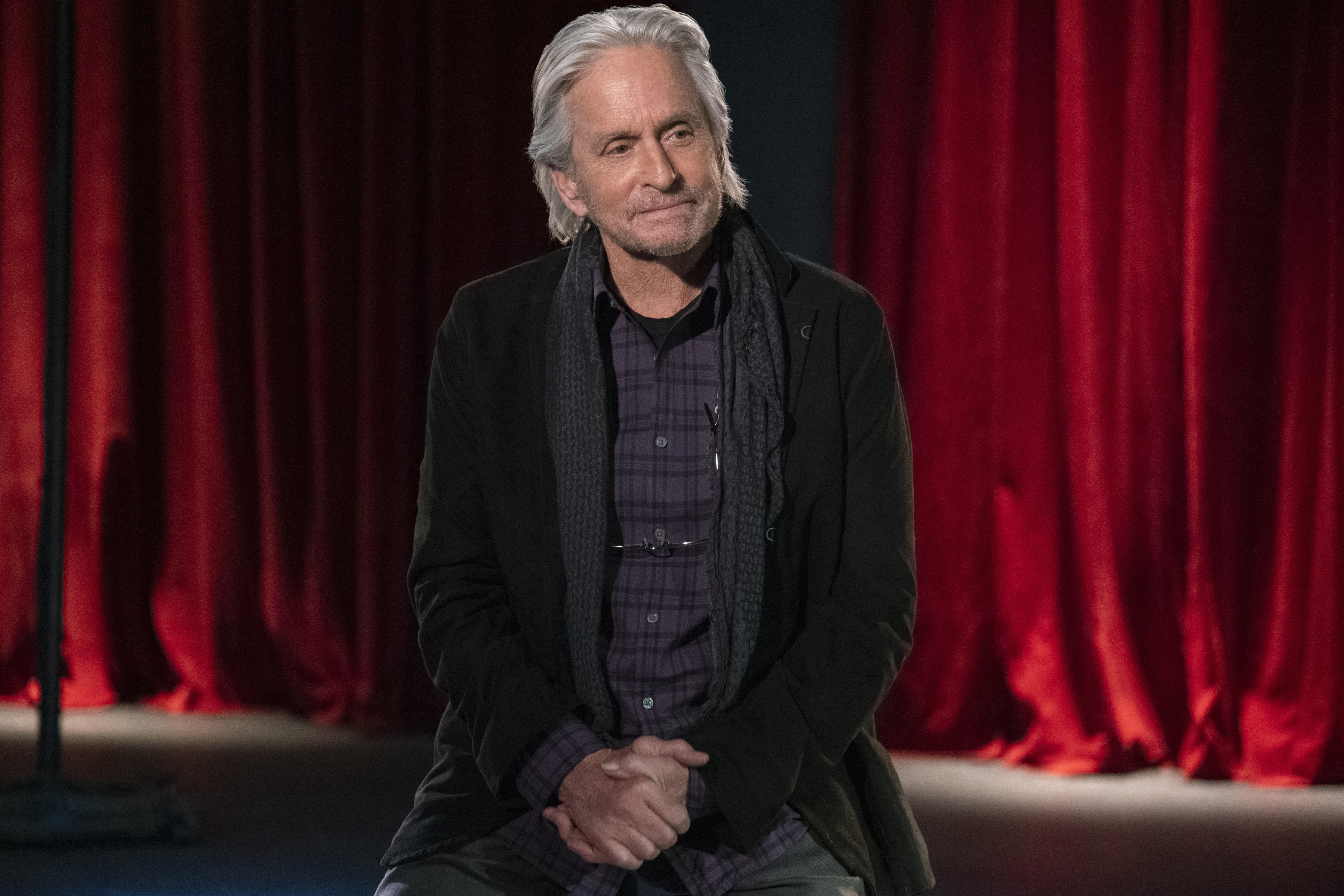 a man sitting in front of a red curtain with his hands folded