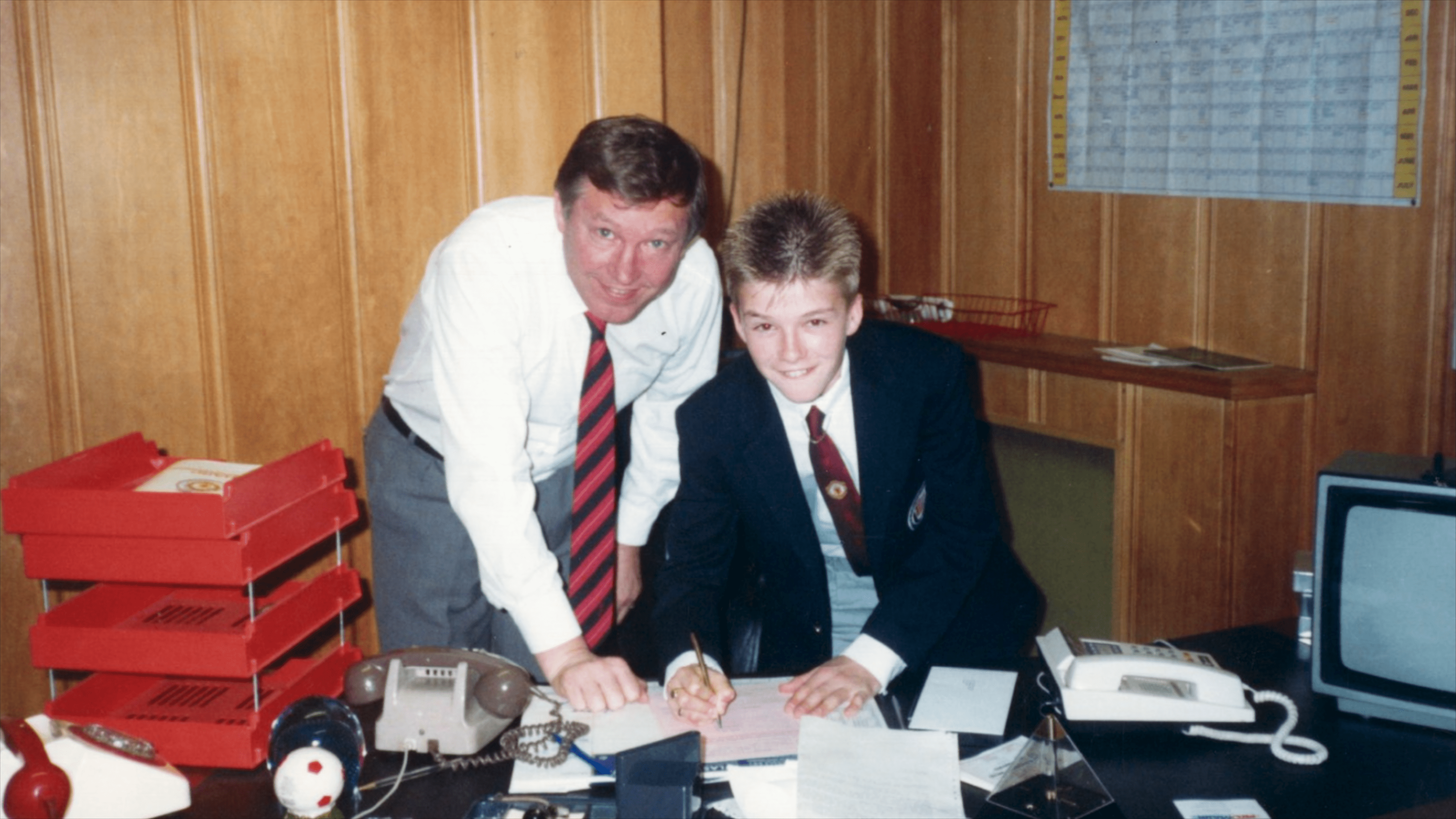 a man stands next to a boy who is signing a document