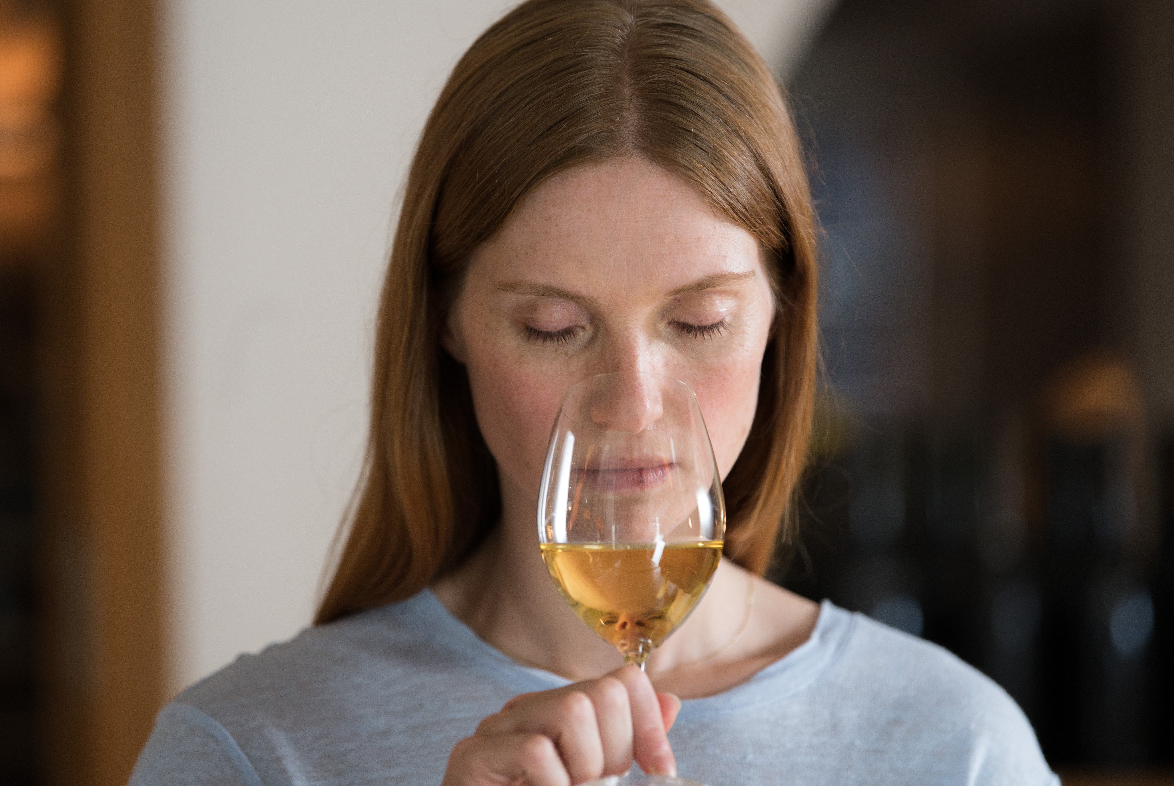 a woman is smelling a glass of wine with her eyes closed