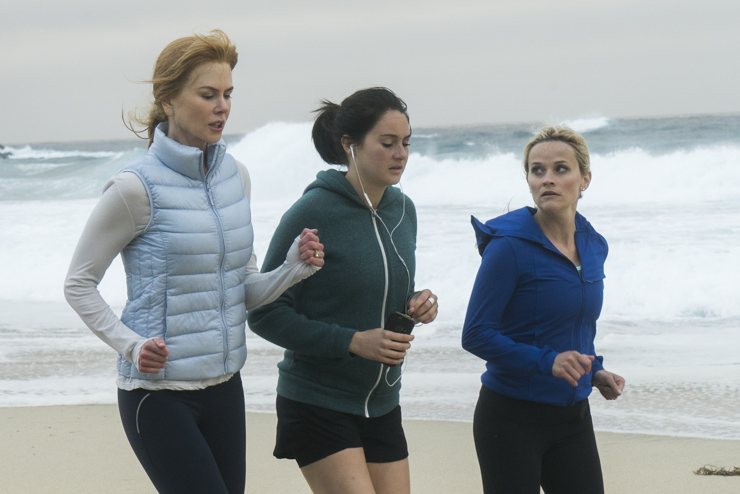 three women are jogging on the beach with one wearing headphones