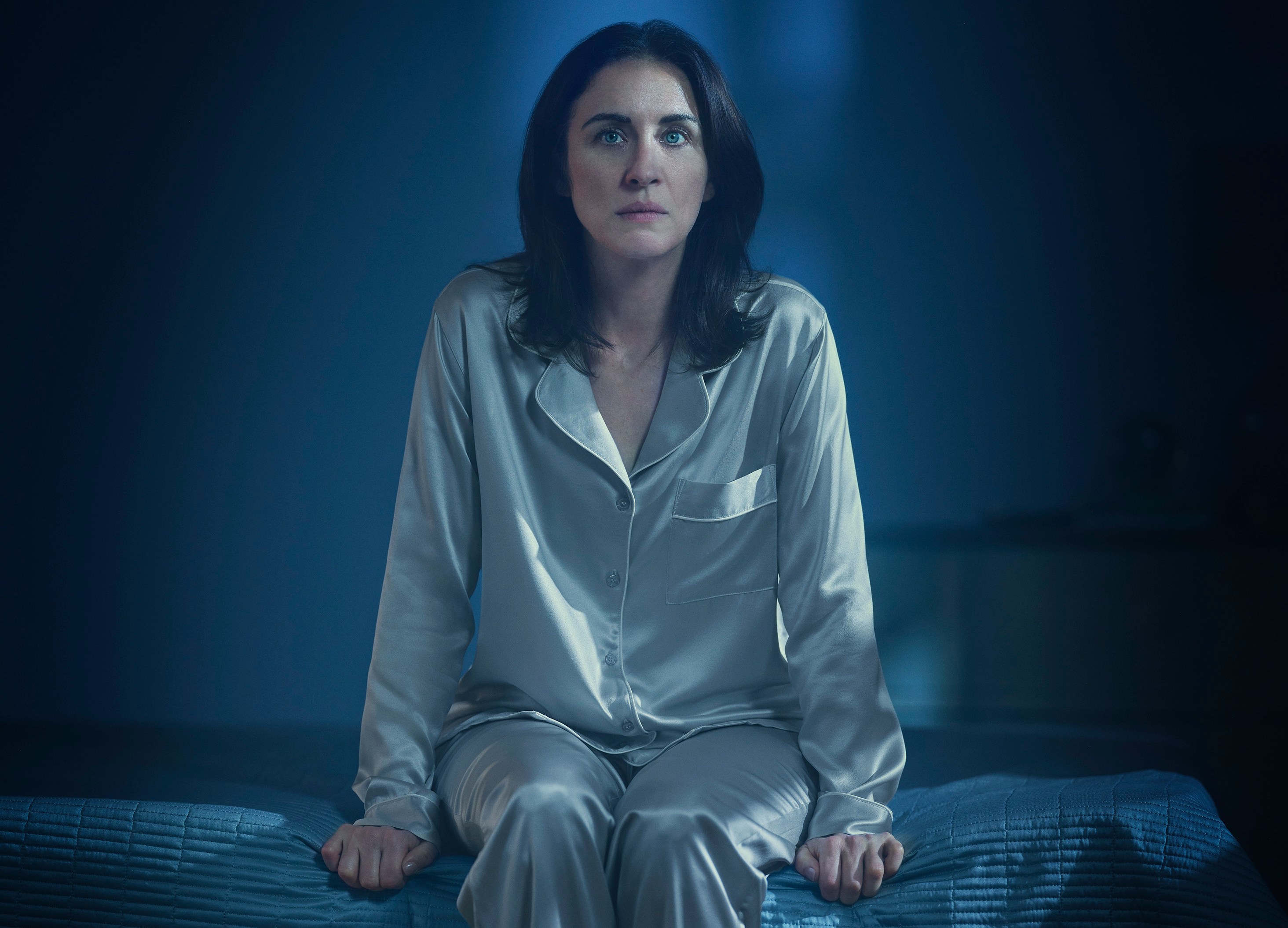 a woman in pajamas sits on a bed in the dark