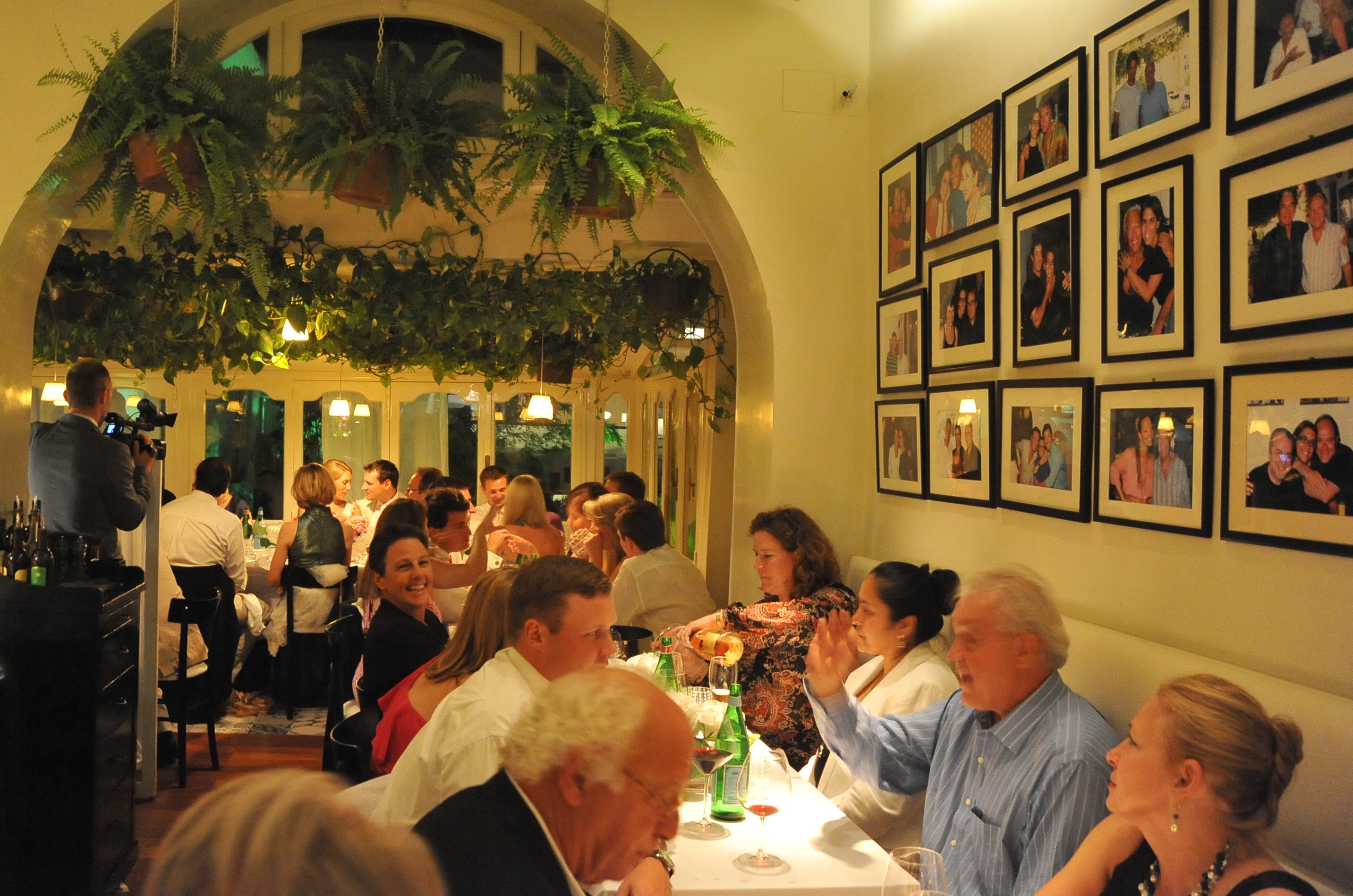 Dinner party at a restaurant with hanging plants and framed photos on the wall.