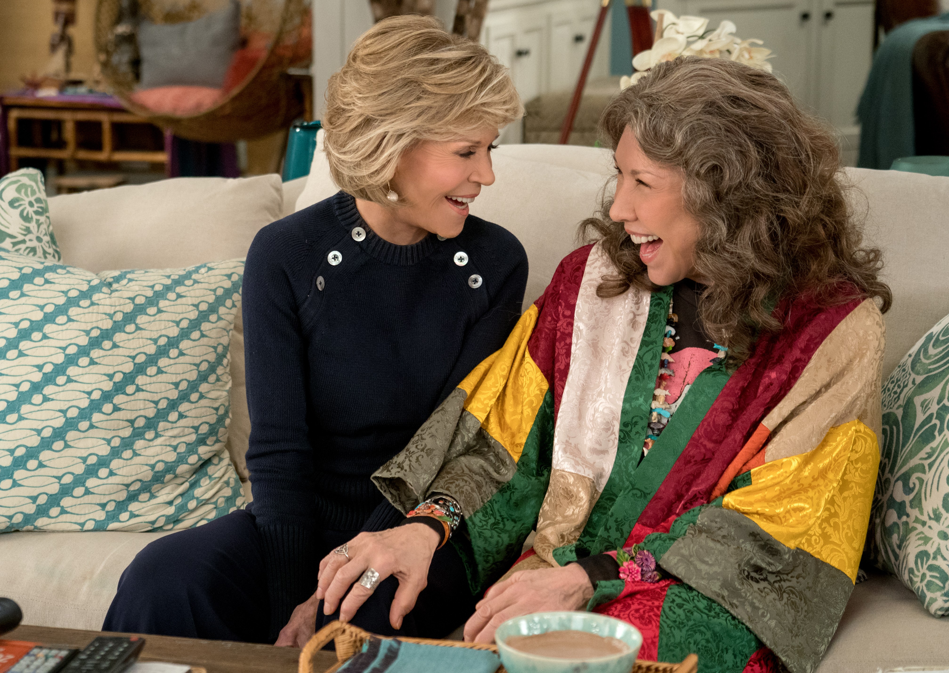 two women are sitting on a couch and laughing