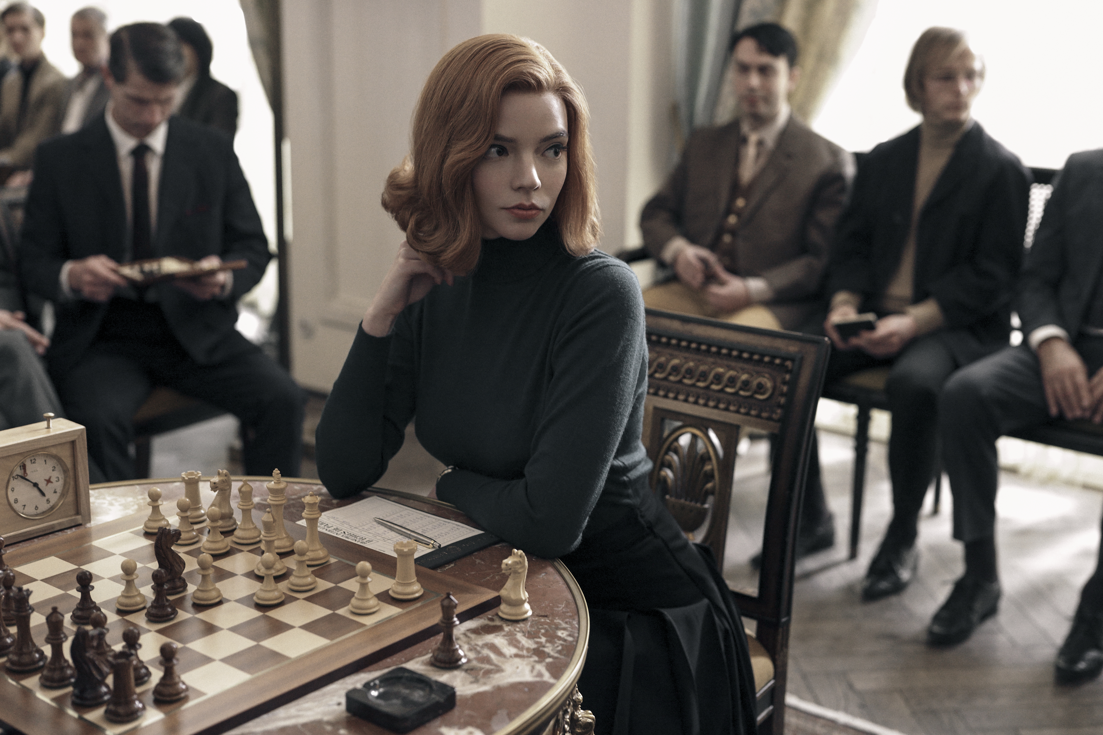 a woman sits at a table with a chess board and a clock on it