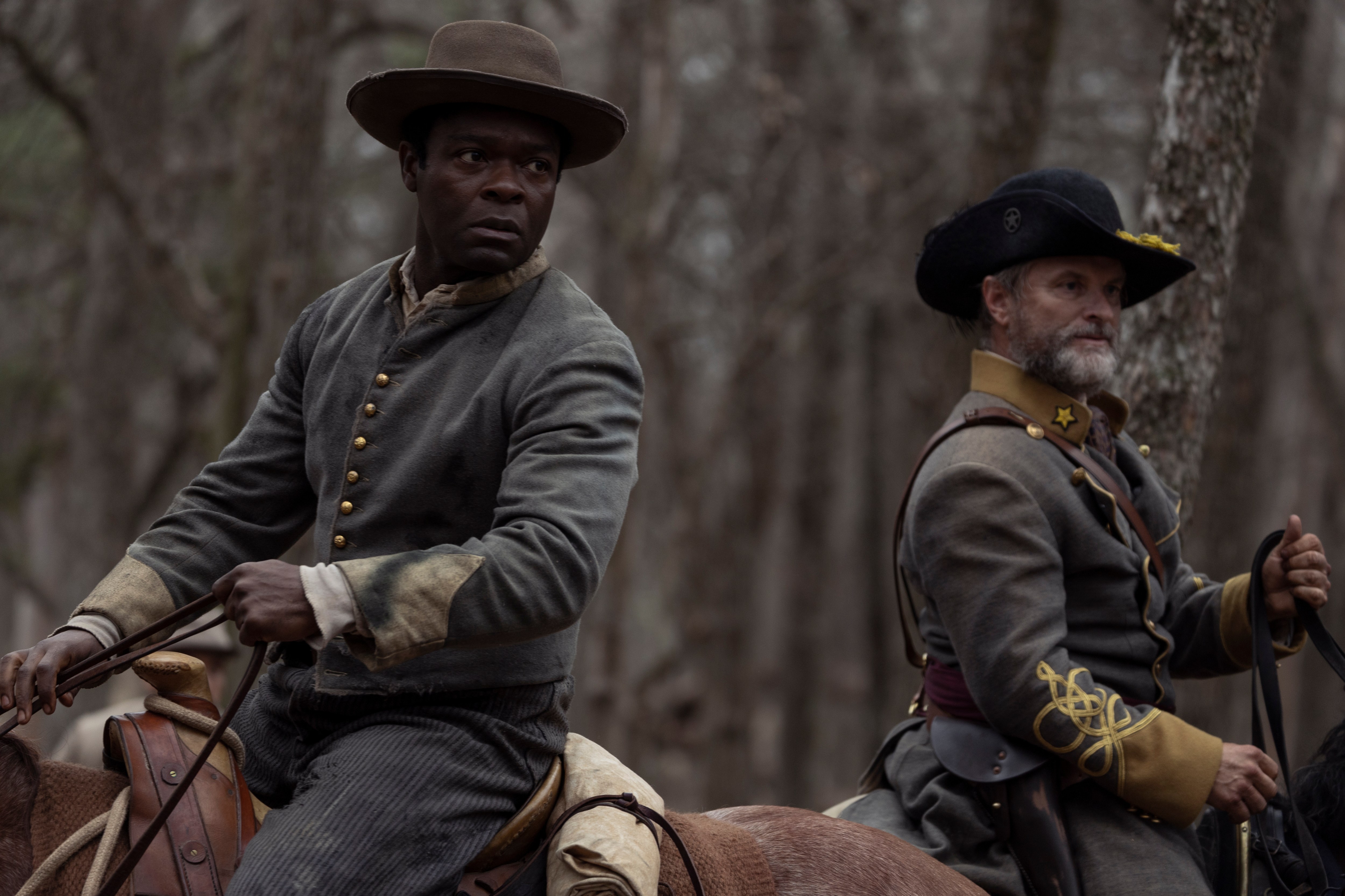 two men in military uniforms are riding horses in the woods