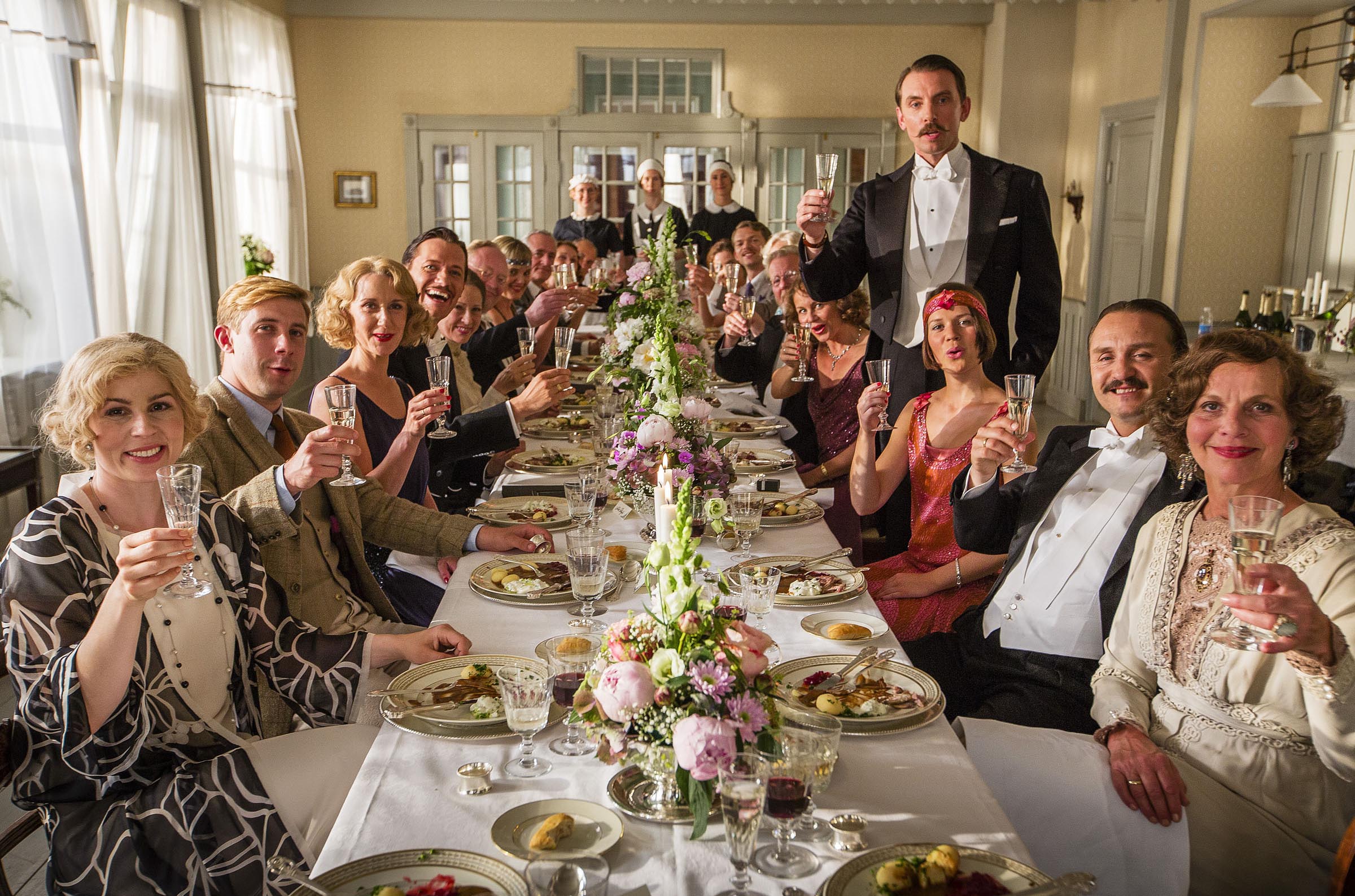a group of people sitting at a long table toasting with champagne glasses