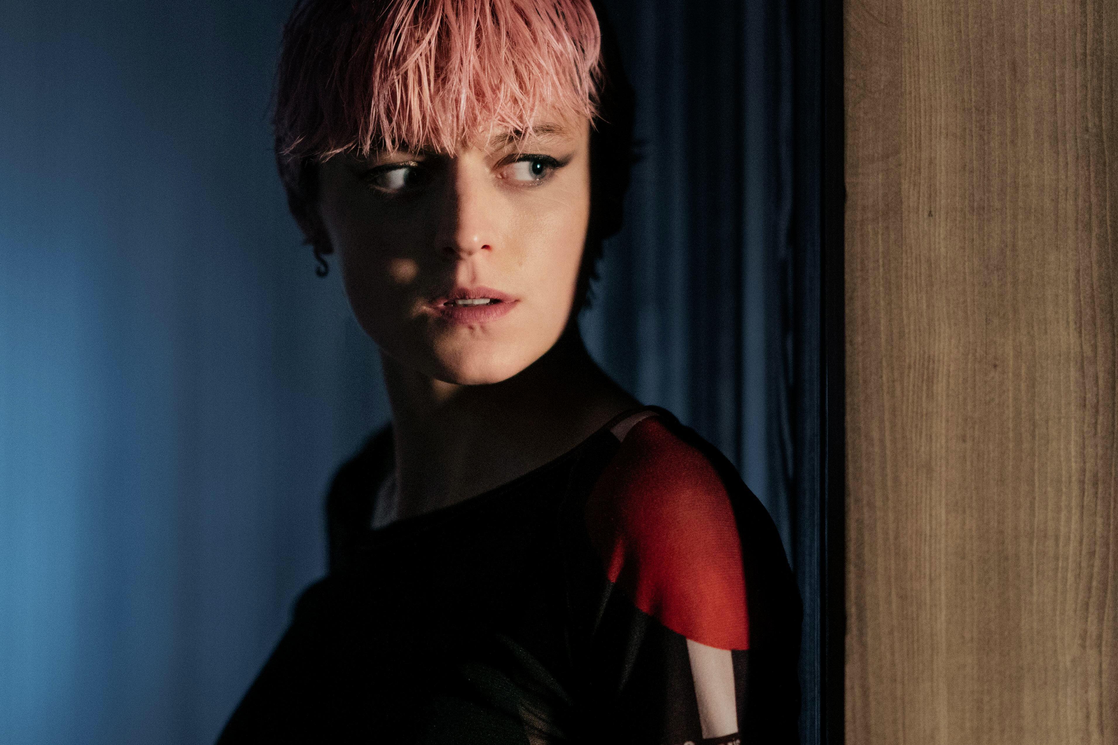 a woman with pink hair is standing in a dark room