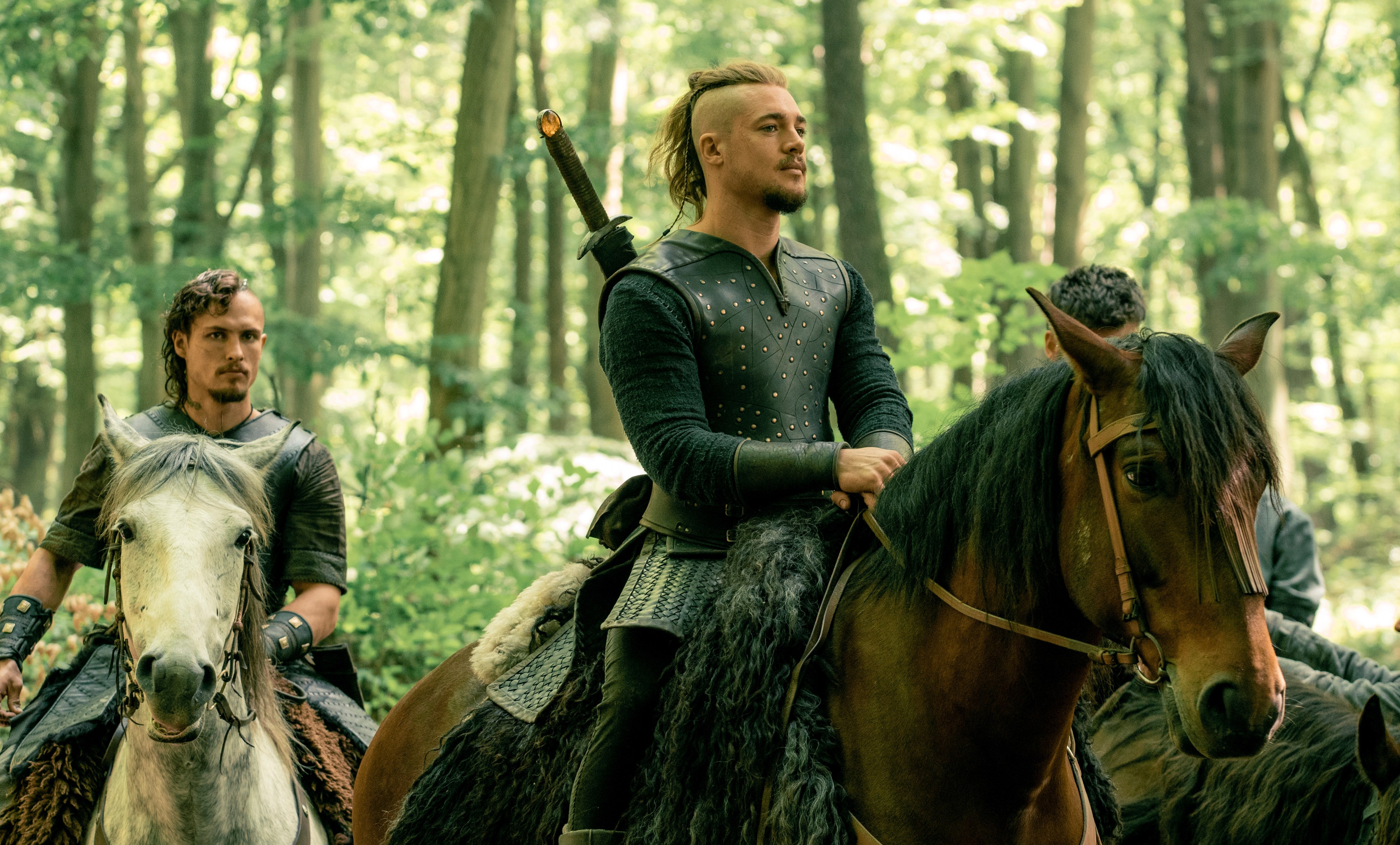 Uhtred and Sihtric on horseback in a forest.