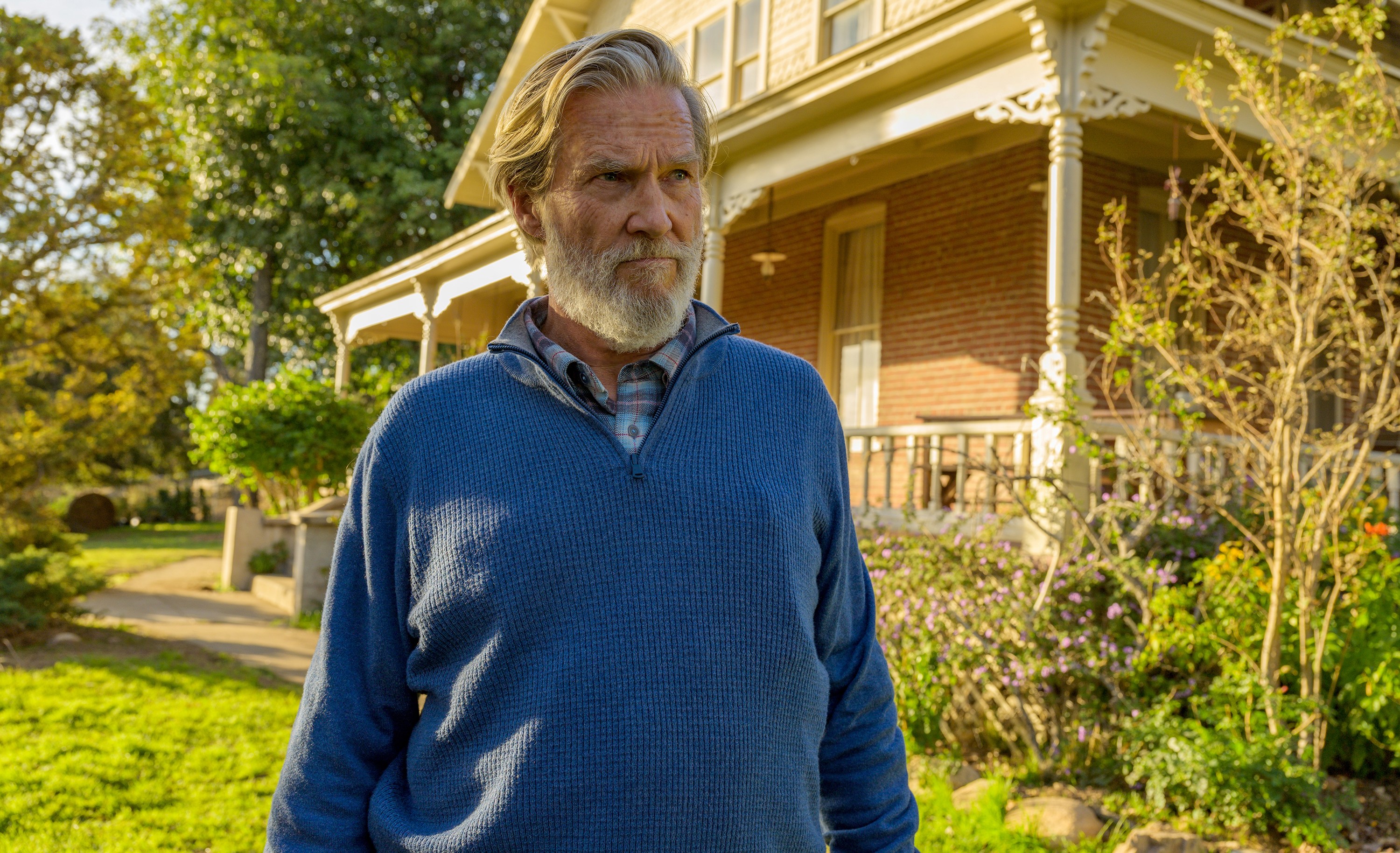 a man in a blue sweater stands in front of a house