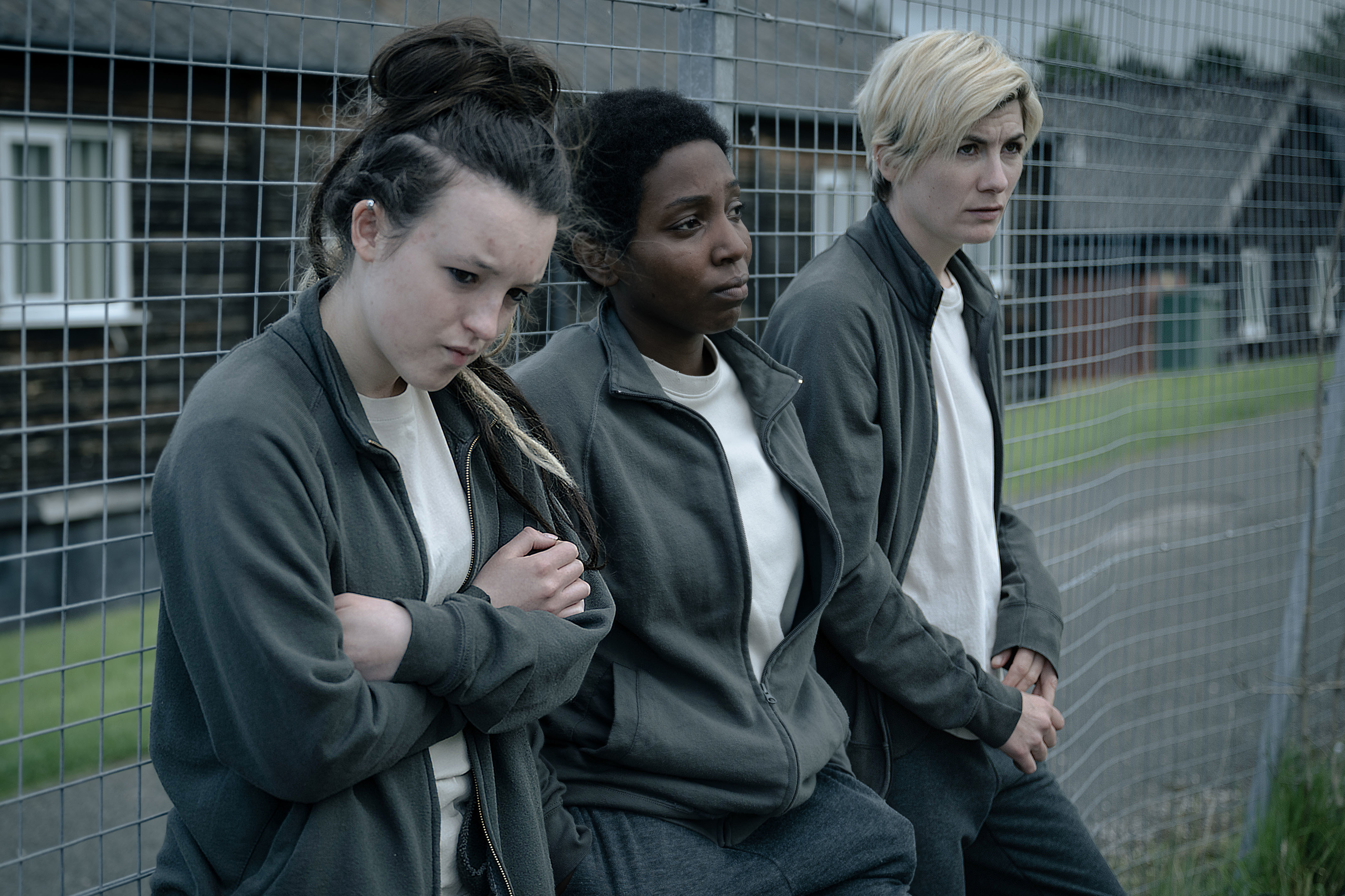 three women standing next to each other in front of a fence