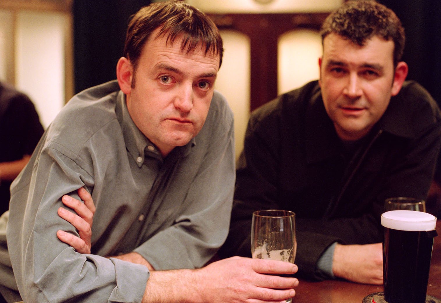 two men sit at a table with a glass of beer that says guinness on it