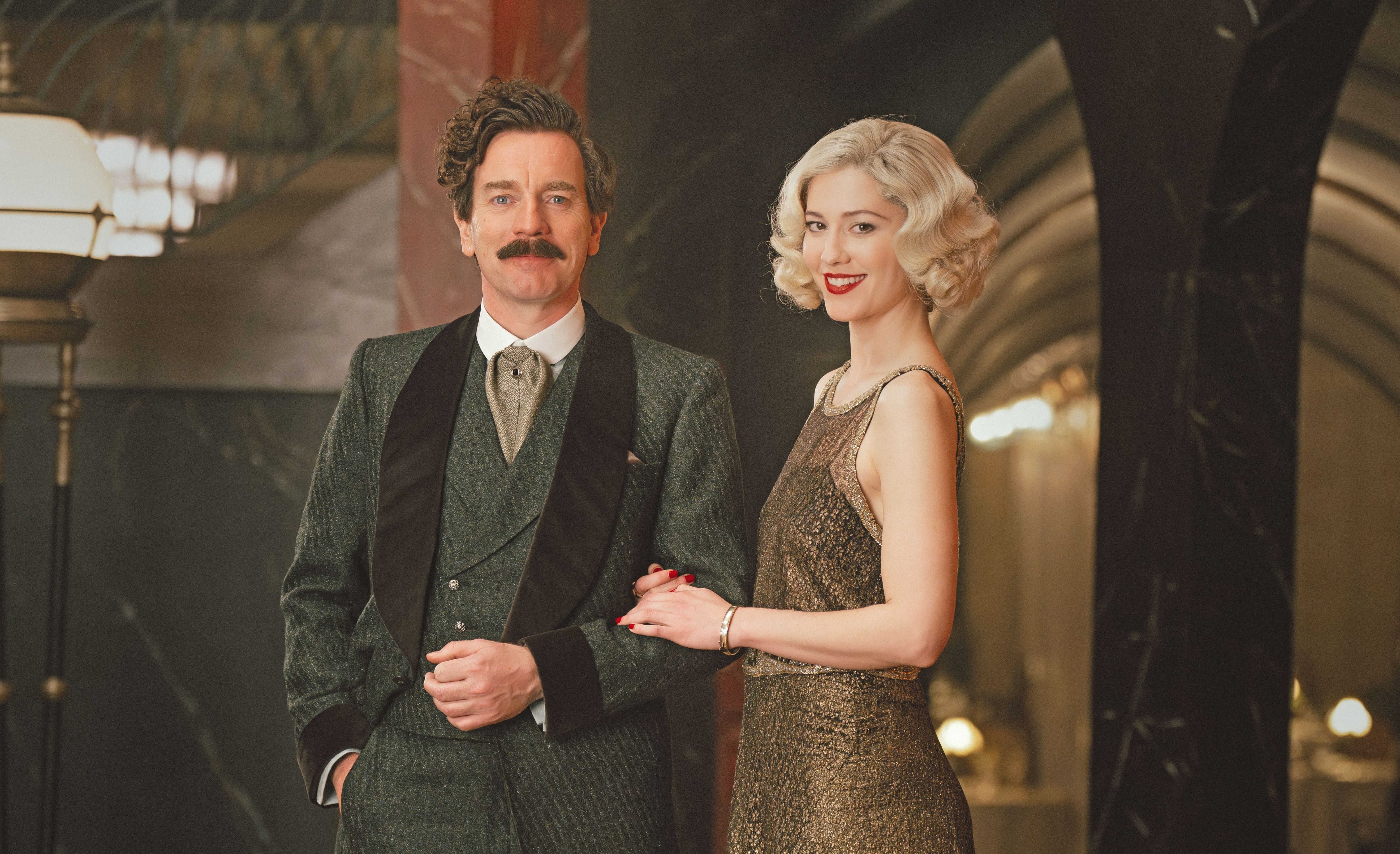 a man in a suit stands next to a woman in a gold dress