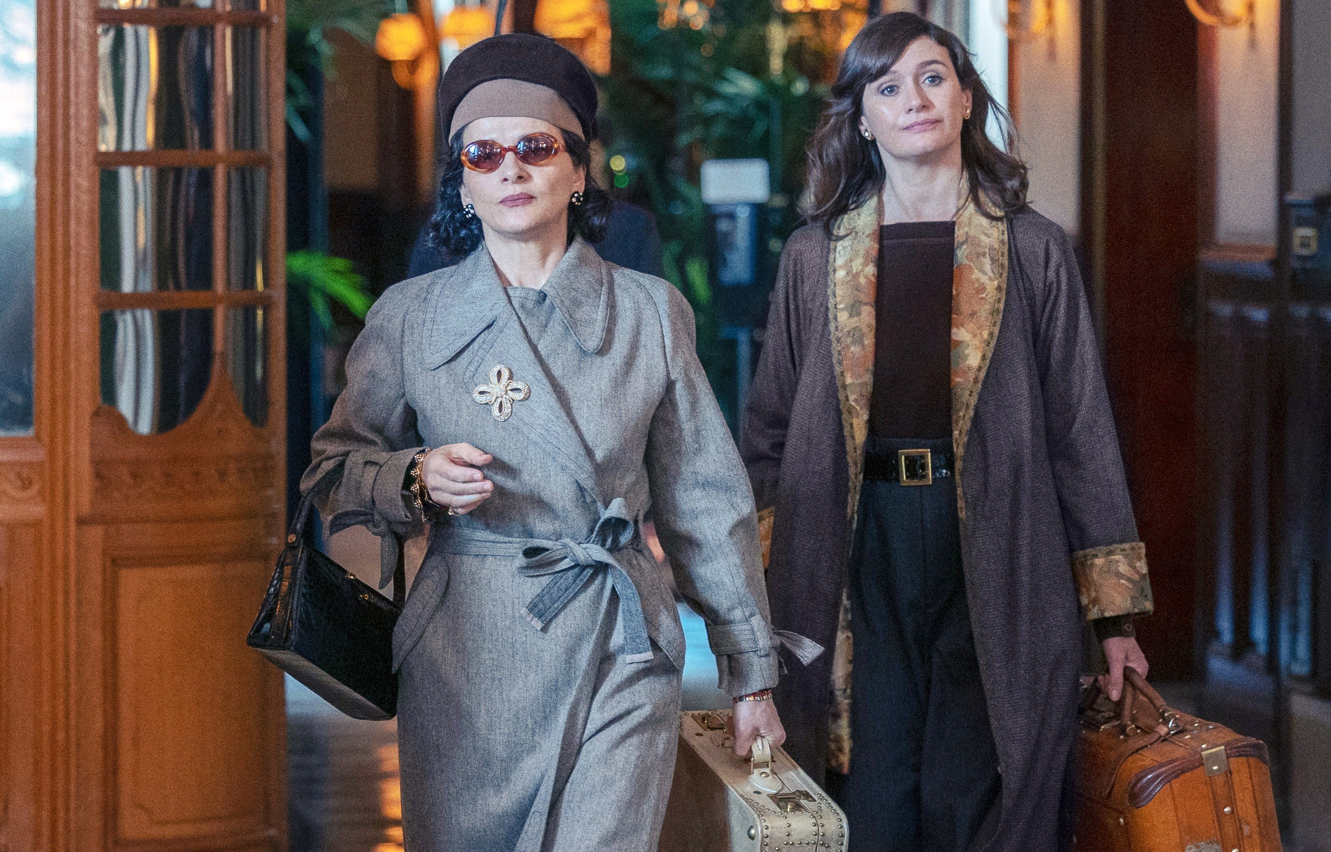 two women are walking down a hallway carrying suitcases