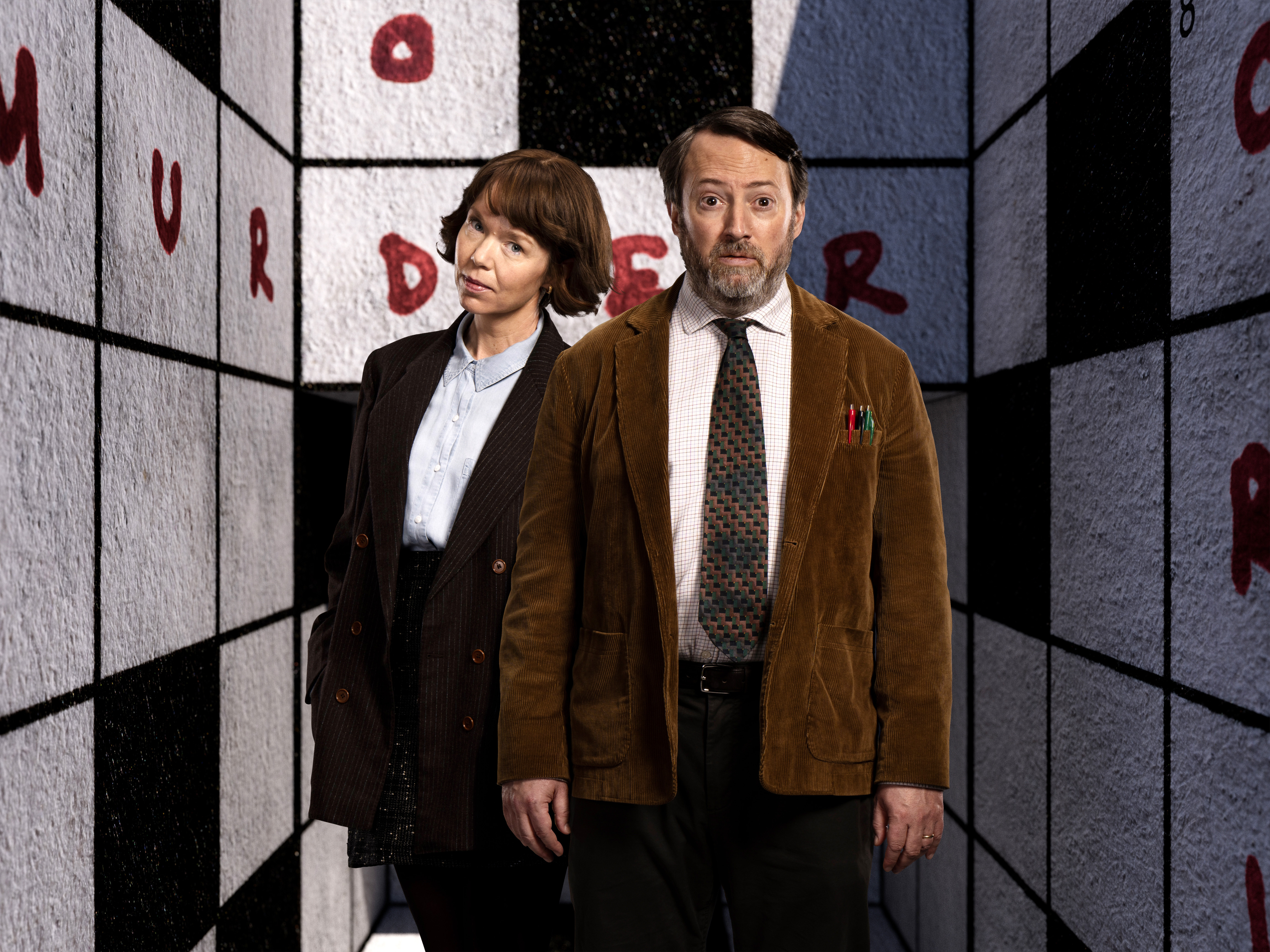 a man and a woman are standing in front of a wall that has the letter r on it