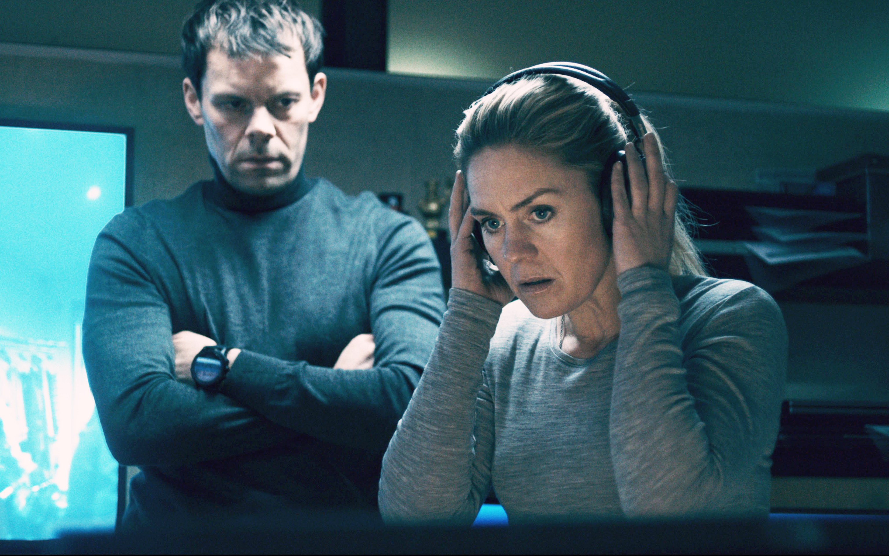 a woman wearing headphones stands next to a man with his arms crossed
