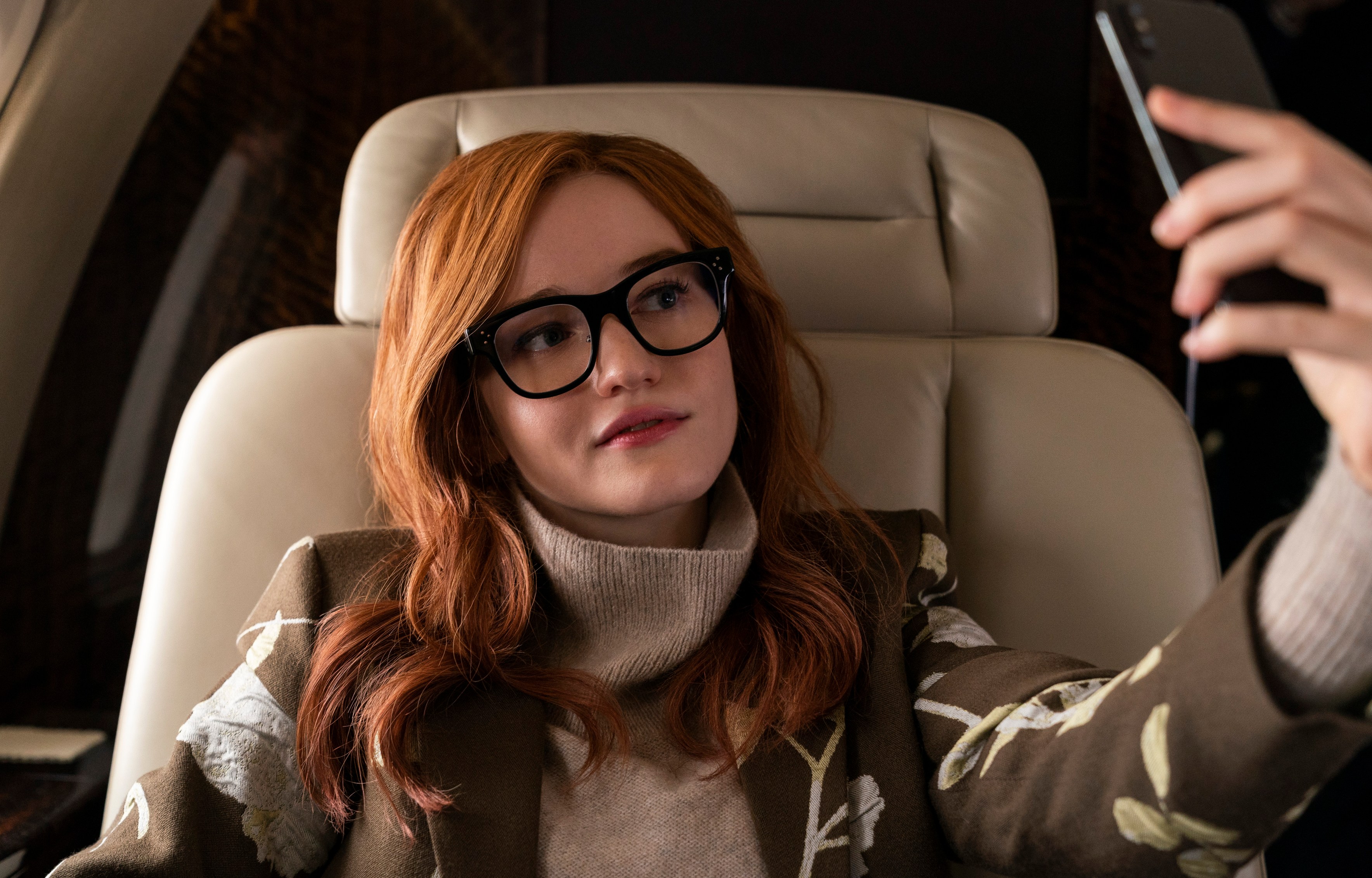 a woman wearing glasses is taking a selfie on a plane