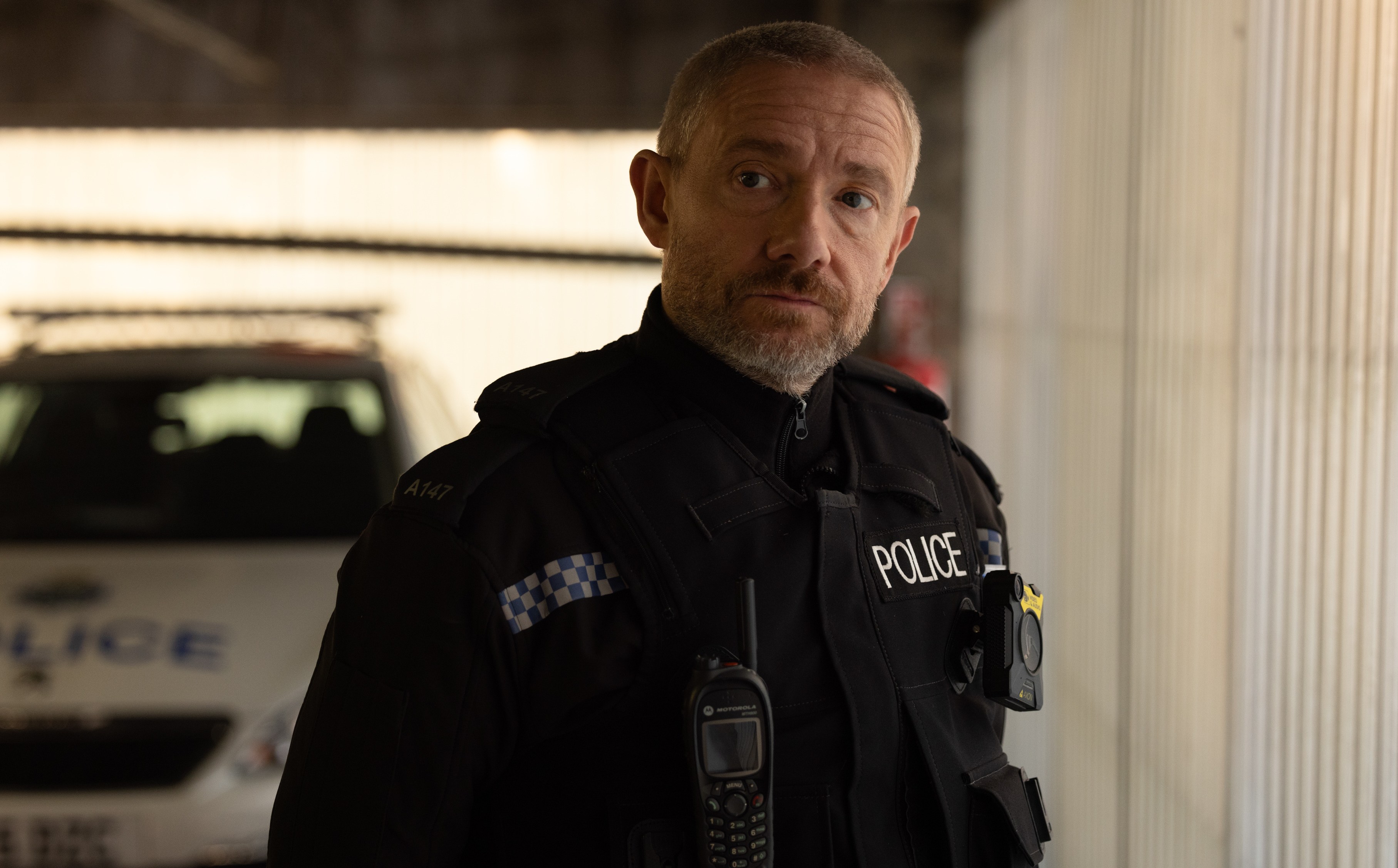 A police officer stands in front of a police car.