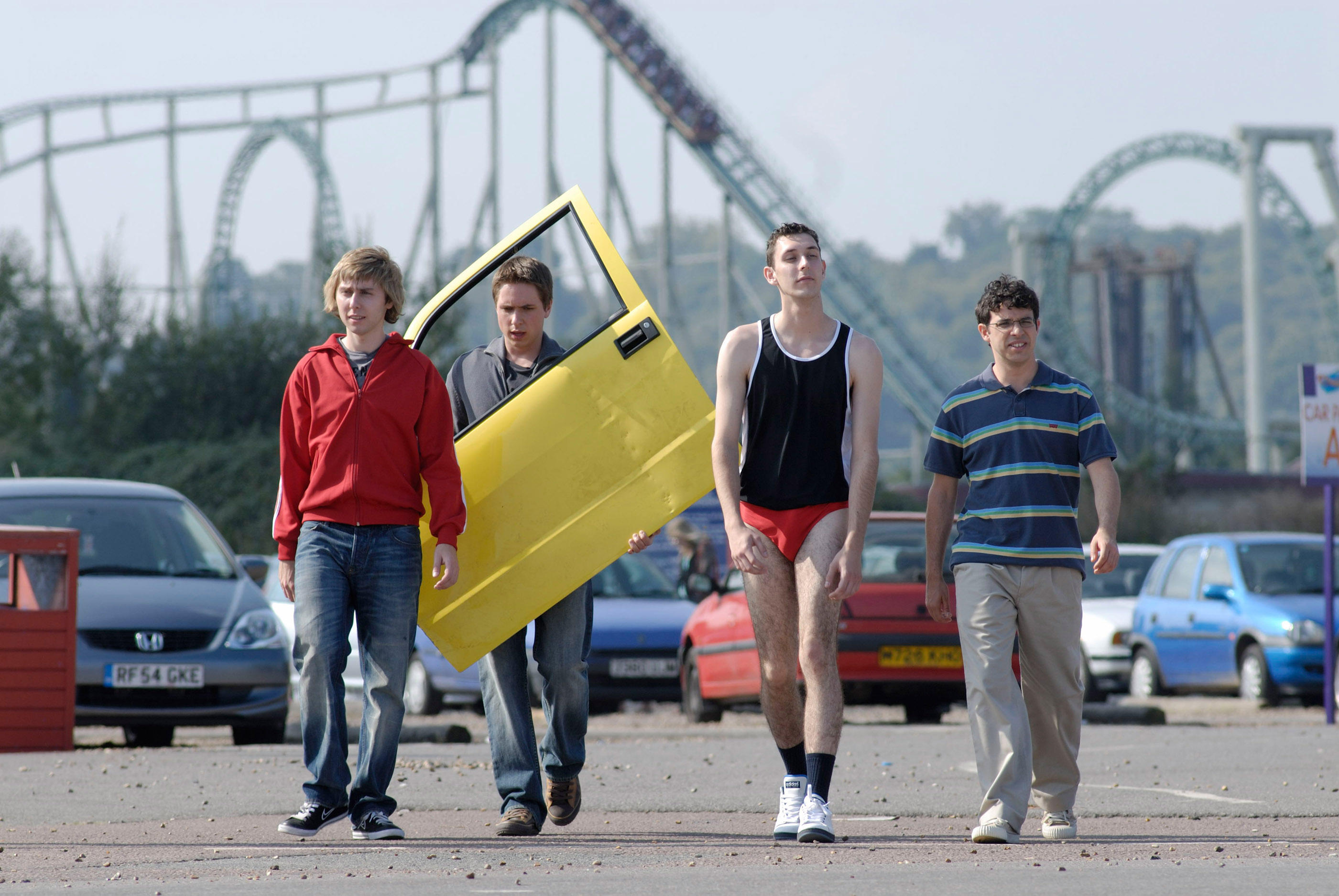 A group of young men are walking in a parking lot with a roller coaster in the background.